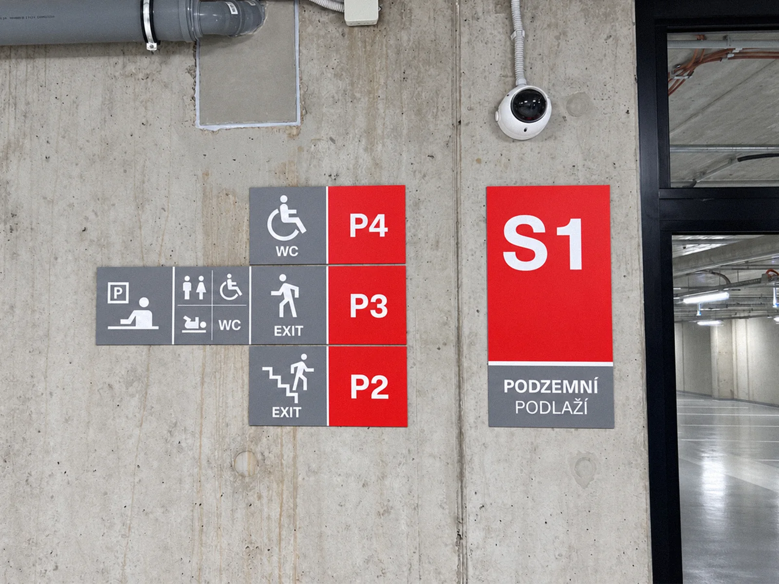 Červené cedule P4 a S1 a šedé směrové tabulky na betonové stěně u schodiště